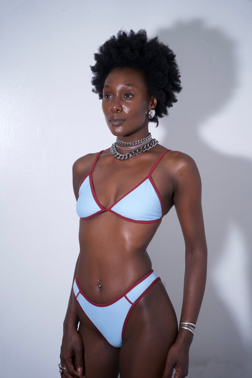 Sandy Bikini Top Blue on a model, featuring light blue fabric with red trim, perfect for beach or poolside.