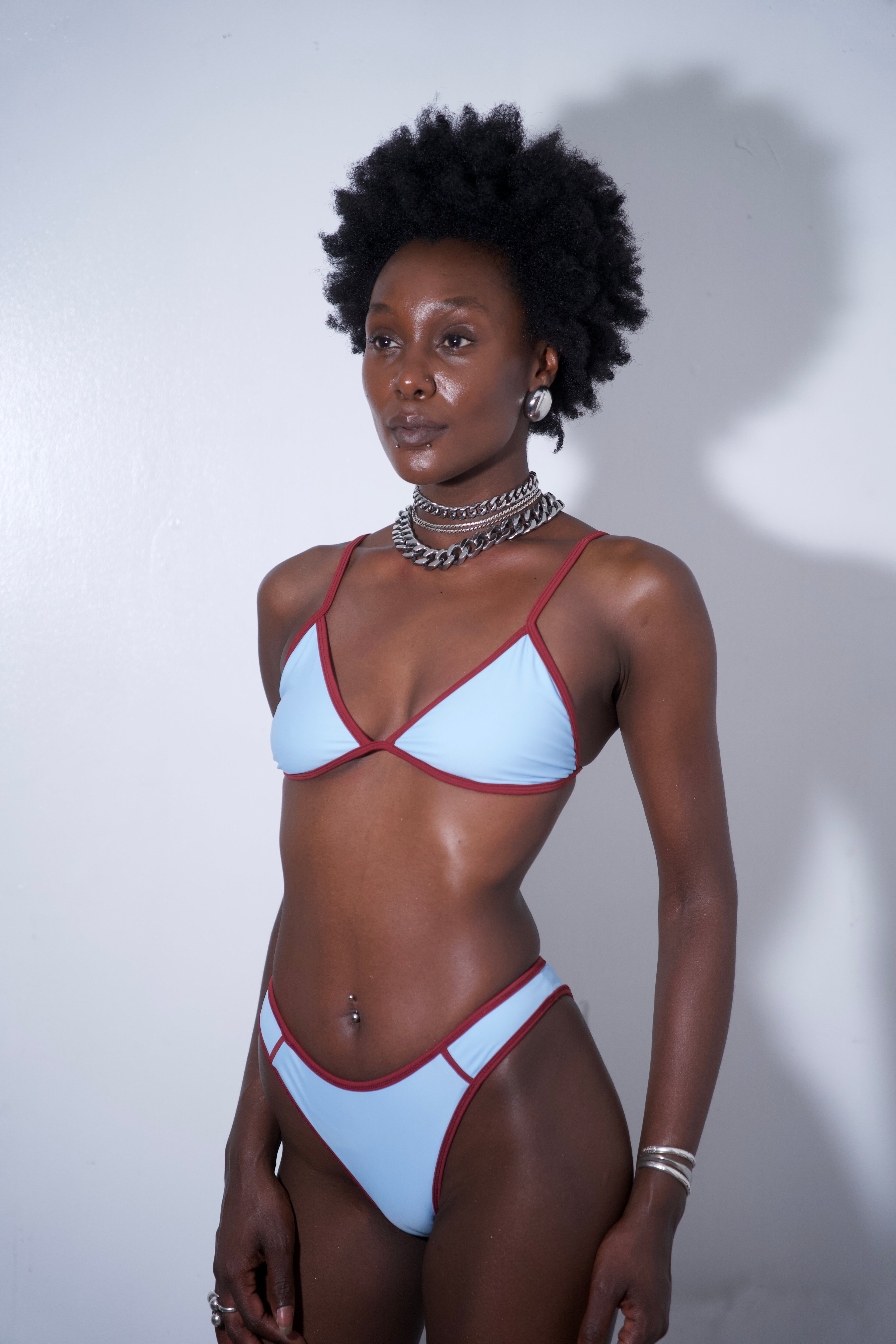 Sandy Bikini Top Blue on a model, featuring light blue fabric with red trim, perfect for beach or poolside.