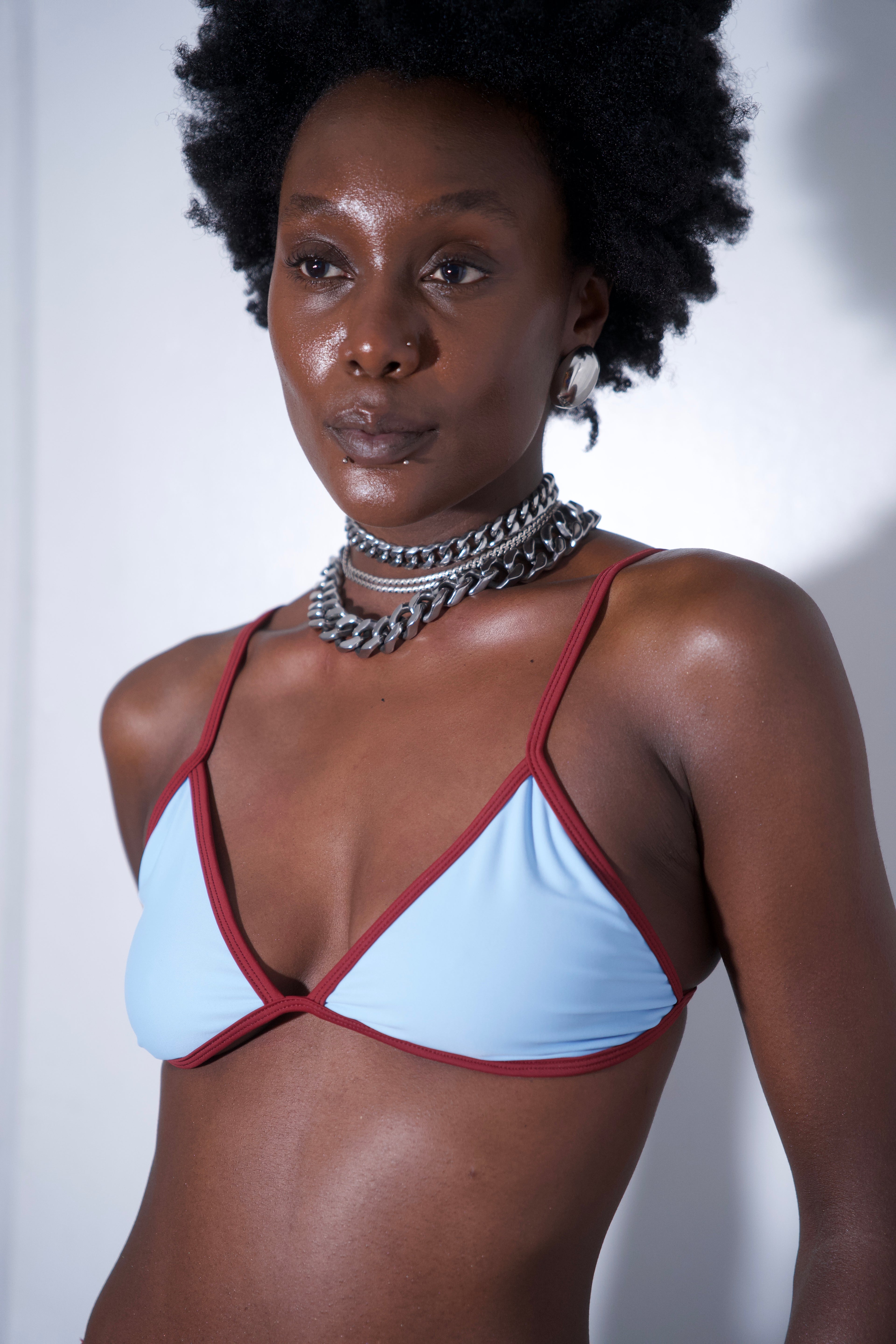 Sandy Bikini Top Blue featuring light blue fabric with red trim and adjustable straps, modeled by a person.